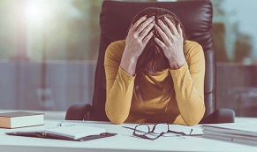 Young woman sitting at desk with head in her hands, frustrated with tax debt.